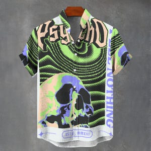 May include: Short-sleeved button-up shirt with a skull graphic. The shirt features the word "PSYCHO" in a bold font, along with the text "BELIEVE NOTHING" and "ESTD.MMXVI". The design incorporates green, black, purple, and peach tones.