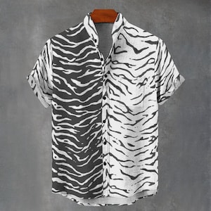 May include: Short-sleeved shirt with a bold zebra stripe design. The shirt is divided vertically, with one side black and the other white. It has a single chest pocket and a mandarin collar. The shirt is hung on a wooden hanger.