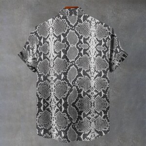 May include: A short-sleeved button-down shirt featuring a monochromatic gray and white snakeskin pattern. The garment has a standard collar, a full-length front button placket, and a repeating reptilian scale print that covers the entire surface.