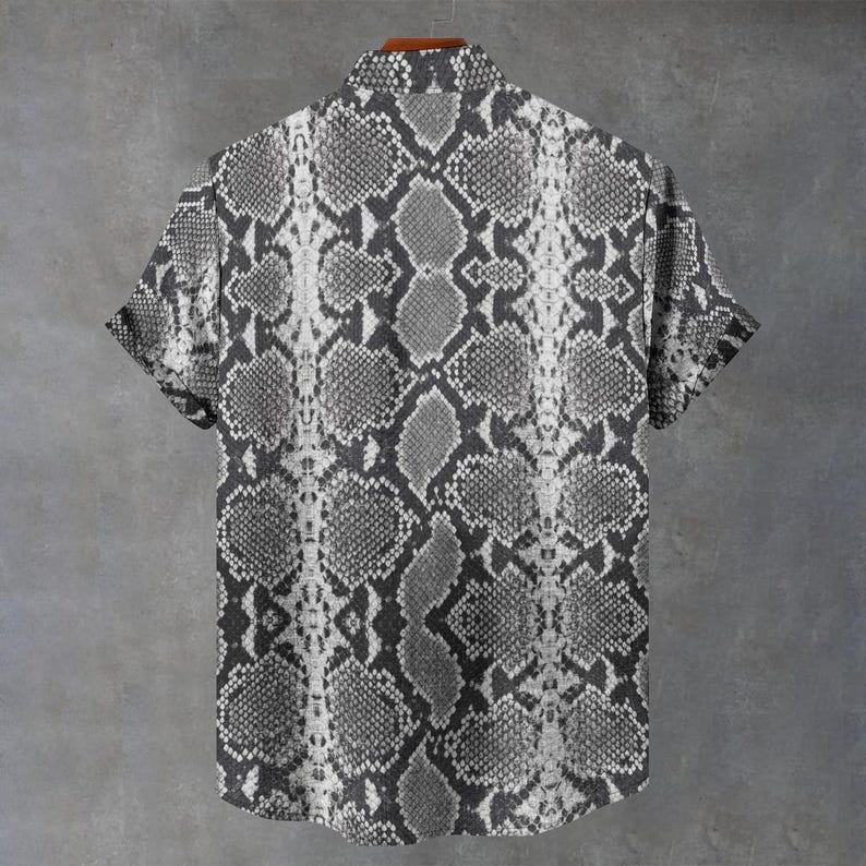 May include: A short-sleeved button-down shirt featuring a monochromatic gray and white snakeskin pattern. The garment has a standard collar, a full-length front button placket, and a repeating reptilian scale print that covers the entire surface.