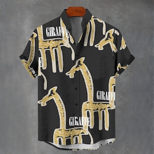 Op de afbeelding: Zwart shirt met korte mouwen met een giraffenpatroon in geel en wit. Het woord "GIRAFFE" is in het wit op het shirt gedrukt. Het shirt heeft een zak aan de linkerkant.