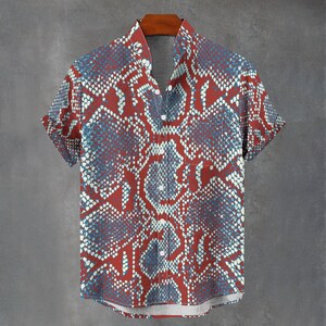 May include: A short-sleeved button-down shirt featuring a repeating snakeskin pattern in shades of red, blue, and white. The shirt has a standard collar, a single chest pocket on the left side, and a straight hemline with white buttons down the front.