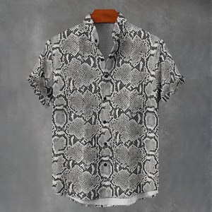 Puede incluir: Una camisa de manga corta con botones y un patrón de piel de serpiente monocromático en gris y blanco. La prenda cuenta con un cuello estándar, una tapeta frontal con botones oscuros y un dobladillo recto, mostrando un estampado de escamas.