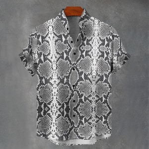 May include: A short-sleeve button-down shirt featuring a monochromatic snakeskin pattern in shades of gray, black, and white. The shirt has a standard collar, a front button placket with dark buttons, and a straight hemline with cuffed sleeves.