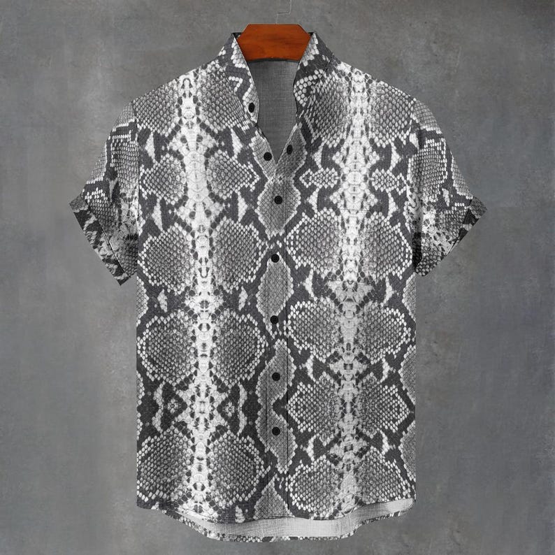May include: A short-sleeve button-down shirt featuring a monochromatic snakeskin pattern in shades of gray, black, and white. The shirt has a standard collar, a front button placket with dark buttons, and a straight hemline with cuffed sleeves.