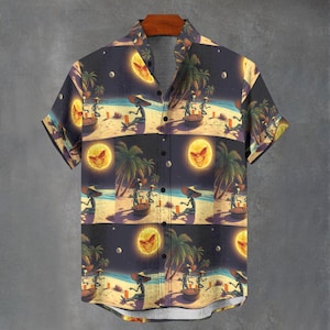 Puede incluir: Camisa de manga corta con botones con un patrón repetido de extraterrestres en una playa por la noche. El diseño presenta una luna llena con una cara, palmeras y extraterrestres sentados en mesas. La camisa es azul oscuro, amarilla y beige.