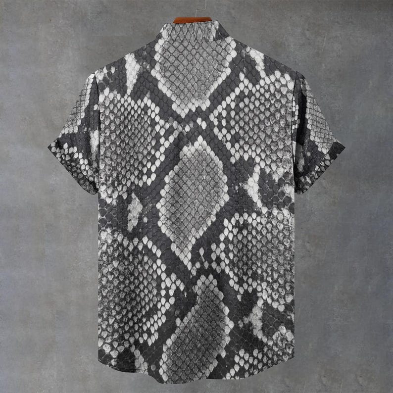 May include: A short-sleeved button-down shirt featuring a monochromatic snakeskin pattern in shades of black, grey, and white. The garment has a standard collar, a straight hemline, and a repeating scale texture across the entire surface.
