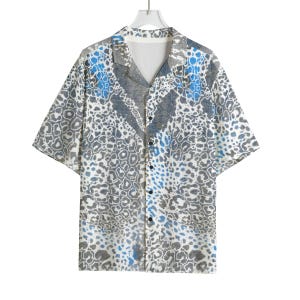 Peut inclure: Une chemise à manches courtes boutonnée avec un motif léopard répétitif dans des tons de gris, de blanc et de bleu vif. Le vêtement présente un col classique, un ourlet droit et une rangée verticale centrale de boutons foncés sur le devant.