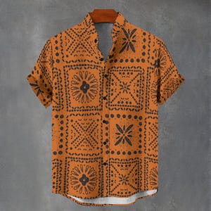May include: Orange short-sleeved shirt with a black geometric pattern. The shirt has a button-down front and a mandarin collar. The design includes floral and square motifs. The shirt is hanging on a wooden hanger.