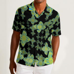 Puede incluir: Camisa negra de manga corta con un estampado floral en tonos verdes y azules. La camisa tiene un cuello clásico y se combina con pantalones blancos. El diseño floral se repite en toda la camisa.
