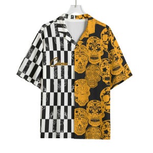 May include: Short-sleeved shirt with a split design. One side has a black and white chequered pattern, the other side features a repeating pattern of yellow sugar skulls on a black background. The word "Calavera" is embroidered on the front.