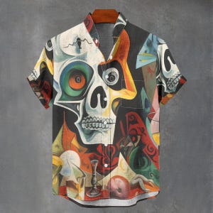 May include: Short-sleeved button-down shirt with a colorful, abstract skull design. The shirt features a V-neck collar and a vibrant mix of colors including white, black, red, yellow, and blue. The artwork is reminiscent of modern art.