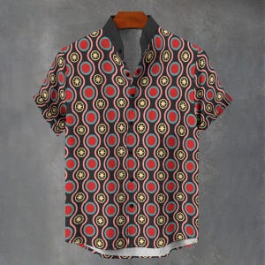 May include: Short-sleeved shirt with a black background and a repeating pattern of red circles, pink rings, and yellow starbursts. The shirt has a black collar and is hanging on a wooden hanger.