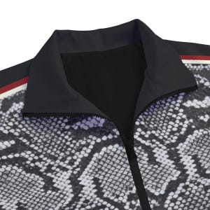 May include: A zip-up jacket featuring a black and white snakeskin pattern across the body. The garment has a solid black collar and a vertical zipper closure. A thin horizontal stripe in red, white, and black accents the shoulder area of the jacket.