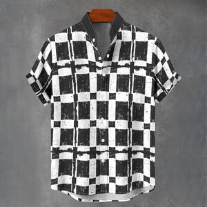 May include: Short-sleeved shirt with a black and white chequered pattern. The shirt features a black collar and white buttons. The fabric has a distressed, textured appearance, giving it a vintage look. The shirt is hanging on a wooden hanger.