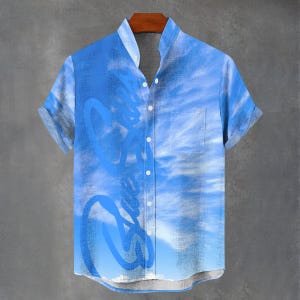 May include: A short-sleeved, button-down shirt in shades of blue, featuring a sky-like pattern with white cloud-like designs. The shirt has a mandarin collar and a single chest pocket. The design includes abstract blue shapes.