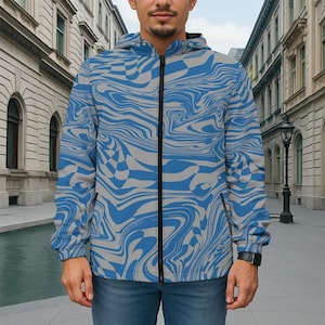 Op de afbeelding: Een jack met capuchon met een blauw en grijs wervelend patroon. De jas heeft een zwarte ritssluiting over de hele lengte en twee zijzakken. Het ontwerp bevat een dambordpatroon, wat een uniek visueel effect creëert. De jas wordt gedragen met een blauwe jeans.