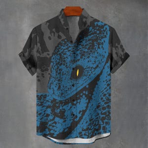 Pode incluir: Camisa de manga curta com um design arrojado de cobra azul e preta. A camisa tem gola mandarim e um corte descontraído. O olho da cobra é amarelo, criando um contraste. A camisa está num cabide de madeira.