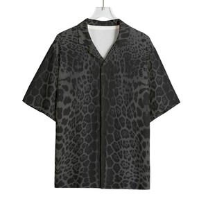 Può includere: Una camicia a maniche corte con un motivo leopardato nero e grigio. La camicia ha un colletto classico e una vestibilità rilassata. La camicia è appesa a un appendiabiti bianco.