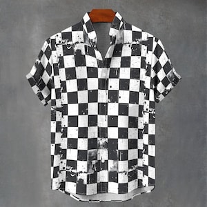 Peut inclure: Chemise à manches courtes avec un motif à carreaux noir et blanc. La chemise a un col classique et une poche poitrine unique. Le design comprend des éclaboussures de peinture pour un look vieilli. La chemise est suspendue à un cintre en bois.