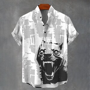 May include: Short-sleeved button-down shirt with a black and white graphic of a snarling dog. The shirt has a gray and white background pattern and a single chest pocket. The shirt is hanging on a wooden hanger.