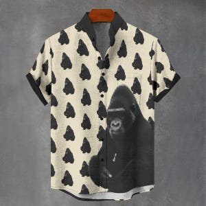 May include: Short-sleeved button-down shirt with a cream background and a repeating pattern of black gorilla silhouettes. A large black and white gorilla graphic is centered on the shirt's front.