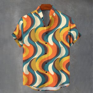 May include: Short-sleeved button-down shirt with a retro wave pattern in orange, yellow, teal, and brown. The shirt has a single chest pocket and is displayed on a wooden hanger against a gray background.