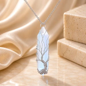 May include: A pendant necklace featuring a translucent, milky white, hexagonal crystal point wrapped in silver-toned wire shaped into a tree design. The pendant hangs from a delicate silver-toned chain, showcasing a smooth, polished finish.