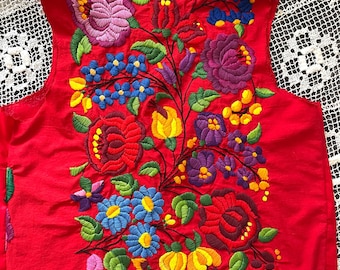 Pode incluir: Um colete vermelho vibrante adornado com intrincados bordados florais. O bordado apresenta uma variedade de flores coloridas, incluindo flores roxas, azuis, amarelas e vermelhas, com folhas verdes. O colete é uma peça de roupa sem mangas.