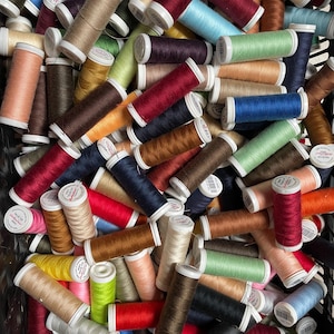 Op de afbeelding: Een verzameling kleurrijke garenspoelen in diverse tinten, waaronder rood, blauw, groen en bruin. De spoelen zijn dicht op elkaar gepakt en tonen een verscheidenheid aan kleuren en texturen, perfect voor naai- en knutselprojecten.