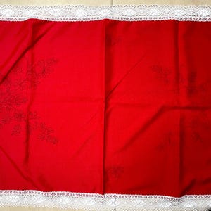 May include: A red tablecloth with white lace trim and embroidered floral designs.
