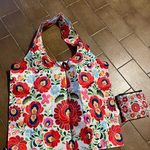 May include: A white tote bag and matching small pouch, both adorned with a vibrant floral pattern. The design features large red flowers with blue and yellow centers, complemented by green leaves and smaller flowers.