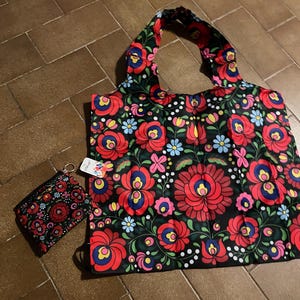 May include: A black tote bag and matching coin purse with a vibrant floral pattern in red, blue, yellow, and pink. The design features large stylized flowers and leaves on a black background. The tote bag has a handle.