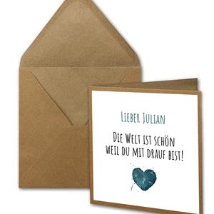 Könnte beinhalten: Eine Karte mit einem braunen Umschlag. Die Karte hat ein blaues Aquarellherz und den Text "Lieber Julian Die Welt ist schön weil du mit drauf bist!"