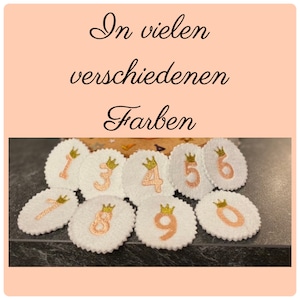 Könnte beinhalten: Weiße Filz-Zahlenaufnäher mit goldenen Kronen und pfirsichfarbenen Zahlen. Die Zahlen 0 bis 9 sind abgebildet. Der Text "In vielen verschiedenen Farben" befindet sich oben im Bild.