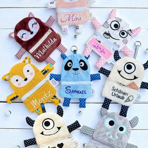 Könnte beinhalten: Eine Sammlung von Plüsch-Reißverschlusstaschen in verschiedenen Tier- und Monsterdesigns. Jede Tasche hat einen einzigartigen Charakter, wie ein Faultier, Fuchs, Panda und Monster, mit gestickten Details und Namen. Die Taschen sind in Rosa, Braun, Gelb, Blau und Grau gehalten.