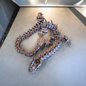 May include: A large, metallic, iridescent dragon sculpture with a long, segmented tail and a detailed head. The dragon is curled up in a circular shape, with its head facing the viewer.