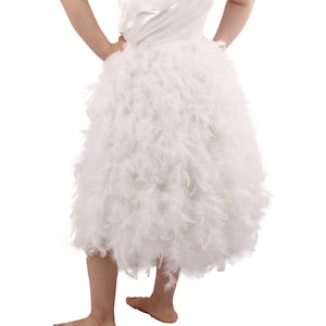May include: A white feather skirt with a fluffy, layered design. The skirt is knee-length and has a soft, flowing texture.