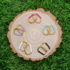 May include: Six pairs of gold hoop earrings with different coloured enamel accents. The earrings are arranged in a circle on a wooden surface.