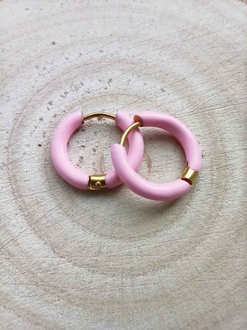 May include: A pair of pink hoop earrings with a gold accent. The earrings are made of a thick, rounded material.