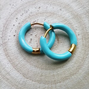 May include: A pair of turquoise hoop earrings with gold accents. The earrings are made of metal and have a smooth, glossy finish.
