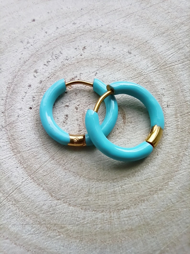 May include: A pair of turquoise hoop earrings with gold accents. The earrings are made of metal and have a smooth, glossy finish.
