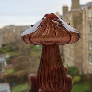 May include: A glass mushroom-shaped vase with a ribbed stem and a wide, flared top. The vase is a deep, rich brown color.