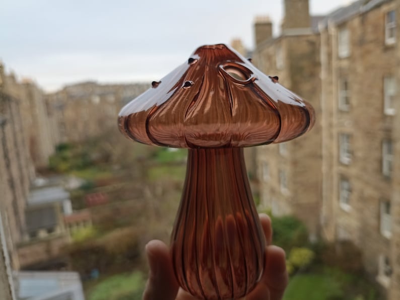 May include: A glass mushroom-shaped vase with a ribbed stem and a wide, flared top. The vase is a deep, rich brown color.