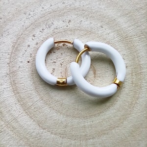 May include: A pair of white hoop earrings with a gold accent. The earrings are made of a thick, rounded material.