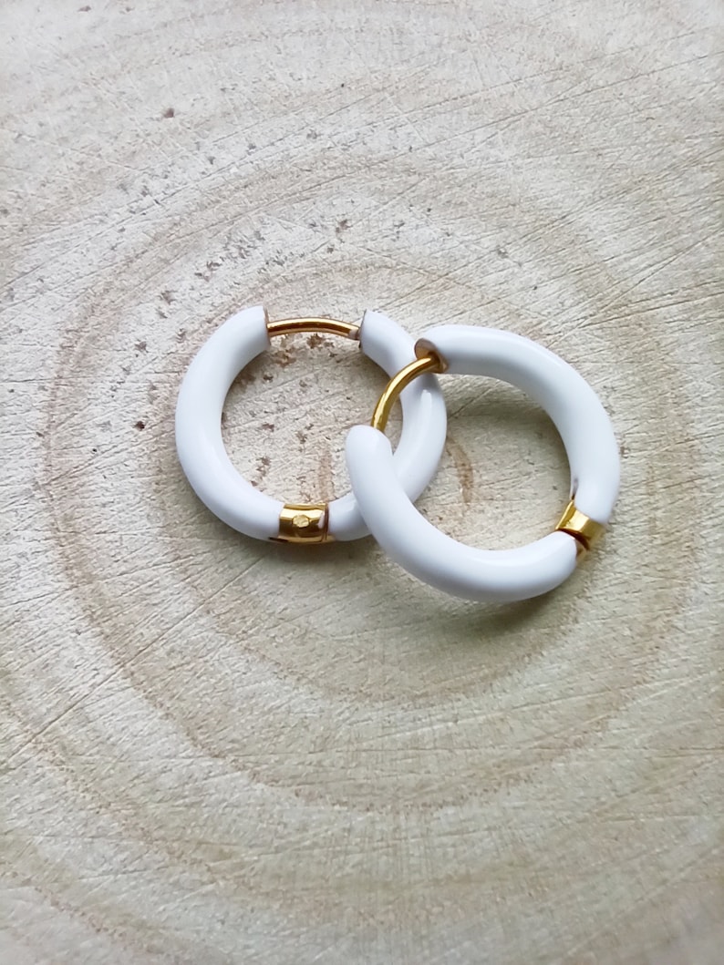 May include: A pair of white hoop earrings with a gold accent. The earrings are made of a thick, rounded material.
