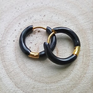 May include: A pair of black hoop earrings with gold accents. The earrings are made of a thick, black material and have a simple, modern design.