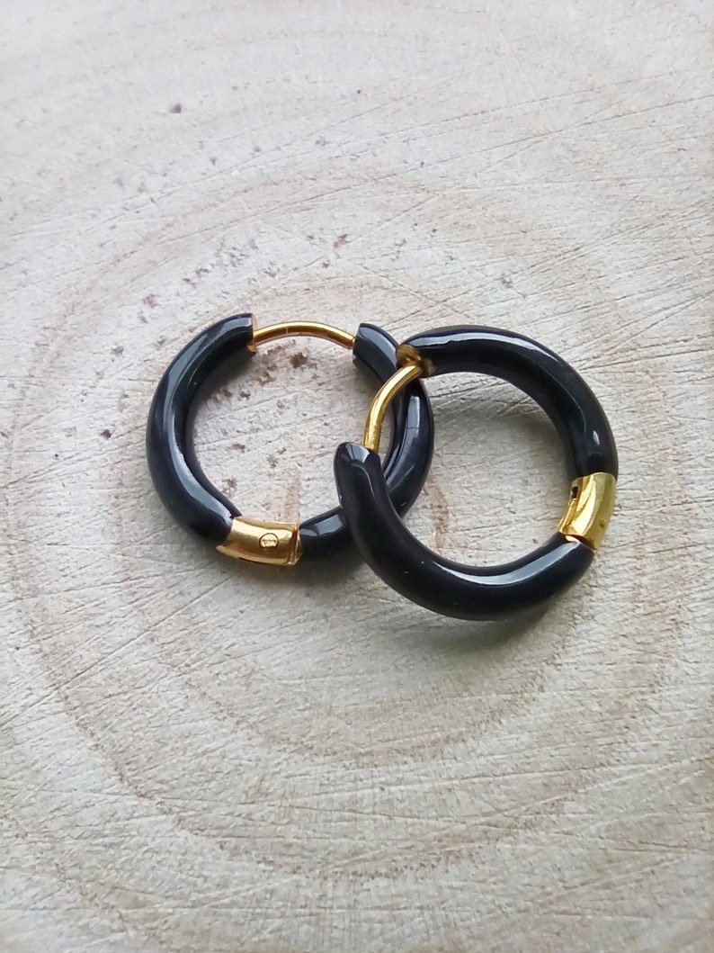 May include: A pair of black hoop earrings with gold accents. The earrings are made of a thick, black material and have a simple, modern design.