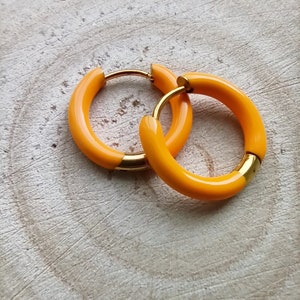 May include: A pair of yellow hoop earrings with a gold accent. The earrings are made of a smooth, shiny material.