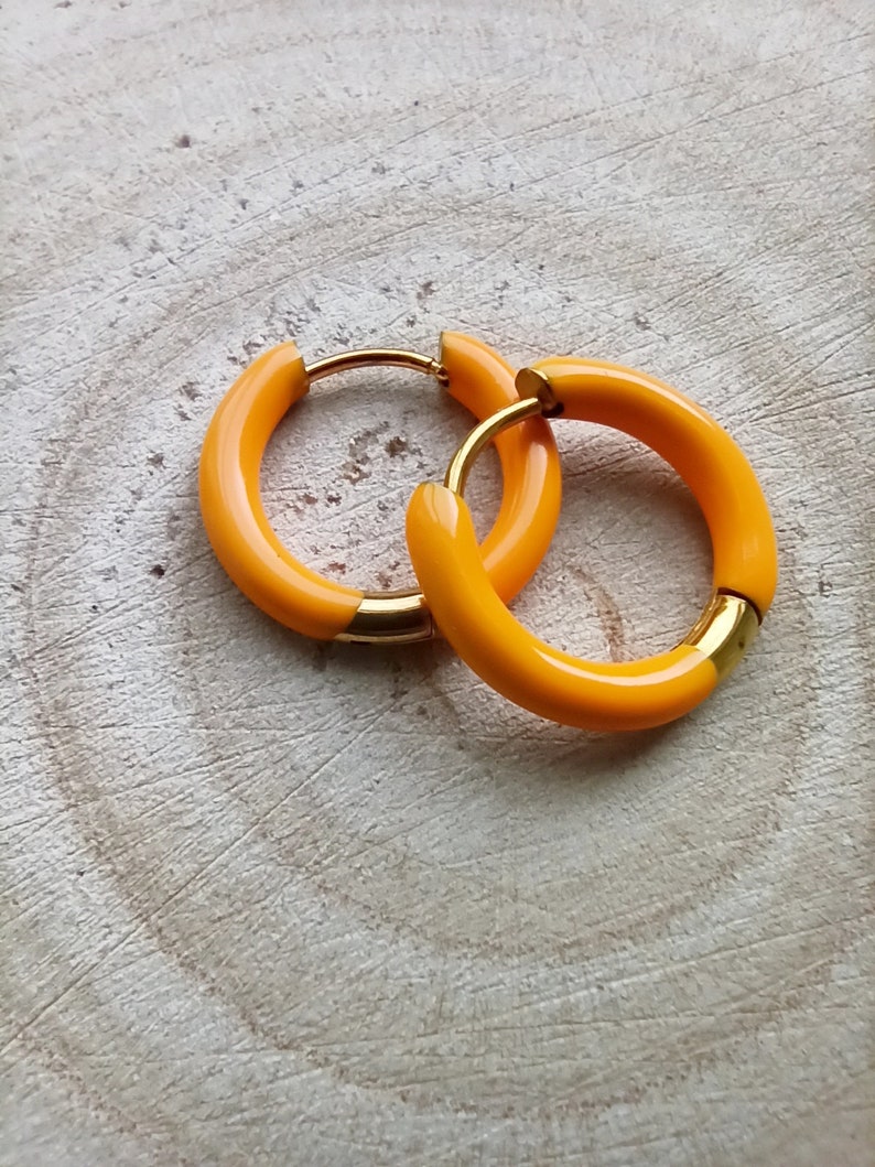 May include: A pair of yellow hoop earrings with a gold accent. The earrings are made of a smooth, shiny material.